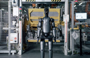 A Figure 02 humanoid robot stands in front of a welding station at a BMW automotive manufacturing plant.