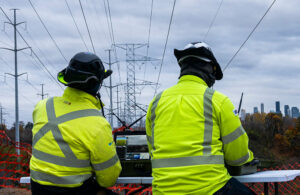 Two people looking at a computer and watching a drone string powerlines.