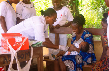 A doctor administering medicine to a baby being held by its mother with a red Zipline box nearby.
